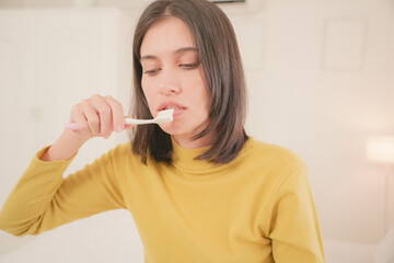 Woman brushing teeth in the morning with natural light, practicing good oral hygiene and healthy...