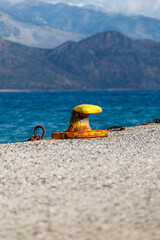 Obraz premium Rusty yellow mooring bollard on a pier with sea and mountain background