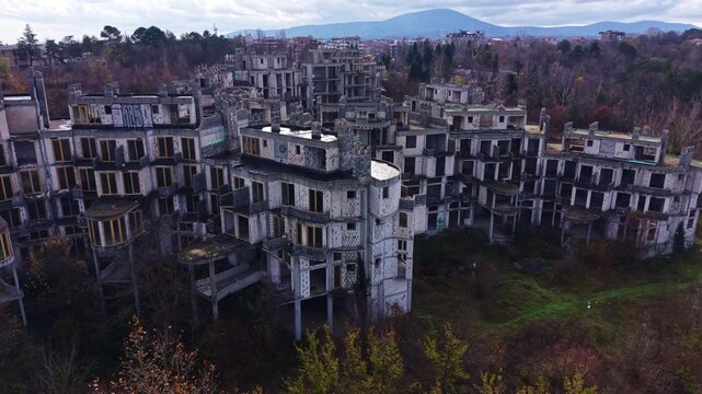 Silent structures stand tall, consumed by greenery as nature retakes its place in the landscape. A distant mountain looms against a dramatic sky, creating a hauntingly beautiful scene.