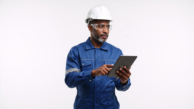 Professional industrial worker in a hard hat using a digital tablet. Focused african american engineer in a blue uniform isolated on a white background with copy space