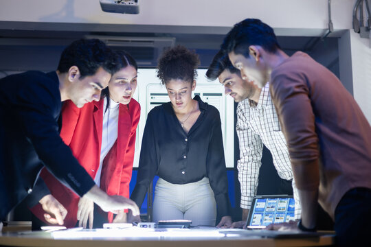 Diverse UX UI design team meeting, collaborating on a web development project. Reviewing blueprints and digital mockups for a creative AI application. Planning for digital marketing strategy