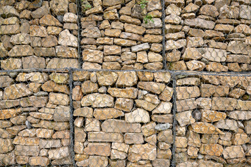 Stone-filled gabion wall made of stacked natural rocks held in metal mesh, creating a rugged architectural texture ideal for backgrounds or construction-themed designs.