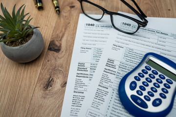 Filling 1040 form for 2026 taxes with calculator, glasses and pen on wooden table