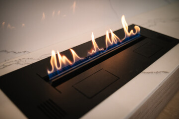 Obraz premium Automatic tabletop biofireplace. Burning eco bio ethanol fireplace built into white marble. Beautiful marble fireplace. Minimalist interior, alternative bio fireplot fireplace on ethanol gas.