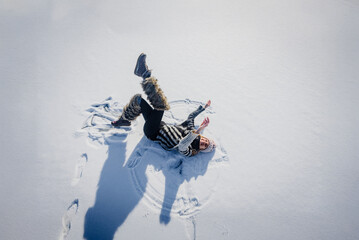 Young beautiful happy woman lying down on white snow. Joyful girl lying on snow, arms outstretched. Winter fun as woman plays on icy surface in nature