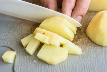 Male cook slicing potatoes with knife on cutting board, closeup photo. Dicing fresh potato with ceramic kitchen knife