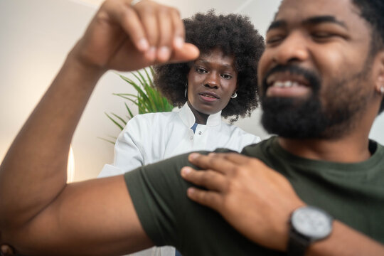 Black female physiotherapist assisting male patient with shoulder exercises in clinic - Powered by Adobe