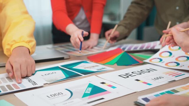 A dynamic group of professionals engaged in a graphic design project showcasing color palettes and logo concepts in a modern office environment. SACTR