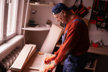 Profession, Small business and hobby concept. Senior elderly carpenter measuring wooden board using tools for work in workshop. Woodworker in carpenter shop