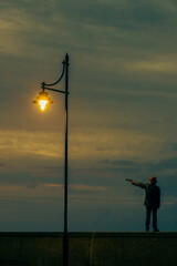 Man with a hat holding gun under lamppost at dawn