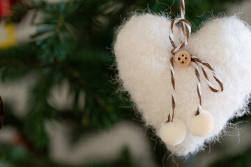 Handmade white felt heart with twine bow on fir; fuzzy texture, selective focus and soft bokeh set a cozy holiday background with timeless Christmas elements for happy new year messages.