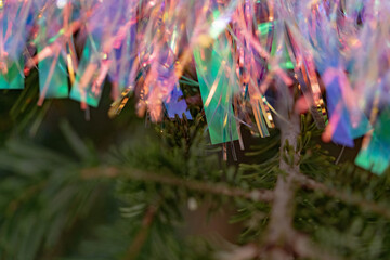 Holographic tinsel with rainbow glints over evergreen; selective focus and soft blur deliver a vibrant holiday background and modern Christmas elements for happy new year visuals.