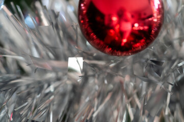 A red glass ball floats above glittering silver tinsel; reflective highlights, selective focus and soft blur deliver an elegant holiday background and Christmas elements for happy new year.