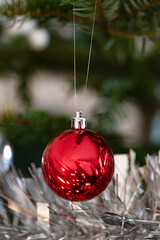 Red mirror bauble suspended above tinsel on fir; selective focus, soft bokeh and clean space shape a festive holiday background and classic Christmas elements for happy new year.