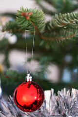 Shiny red ball hangs from evergreen above tinsel; selective focus, soft blur and copy space provide a classic holiday background and Christmas elements for happy new year greetings.