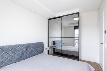 Modern Minimalistic Bedroom Interior with Mirror Wardrobe and Gray Upholstered Bed