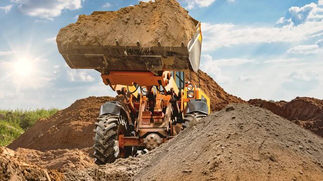 Loader operates at construction site moving dirt while the sun shines. The machine lifts and dumps material onto a pile at the job location.