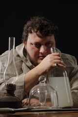 A fat, warlike monk at a table on which stands a bottle of elixir or simply moonshine, a kerosene lamp, some kind of magical utensils and a large two-handed sword