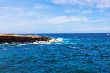 Rocky Arikok National Park coastline with Caribbean Sea waves crashing and blue sky on background. Aruba.