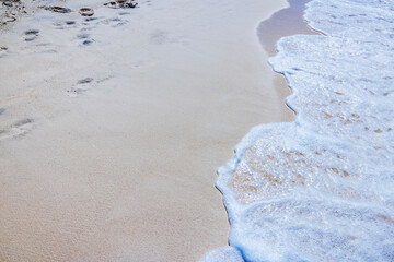 Caribbean wave gently touches clean beach with smooth white sand and fading human footprints. Aruba.