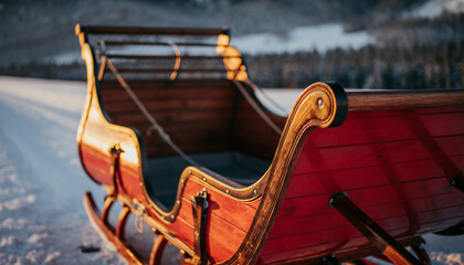 A beautifully crafted traditional wooden sleigh with red accents resting in a serene, sunlit winter wonderland.