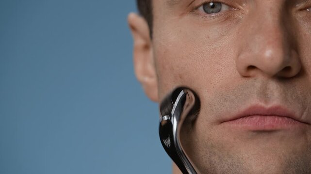 Close up of Caucasian man looking at him, using metal jade roller to massage skin on cheekbones