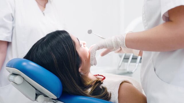 Professional dentist wearing gloves using tools to examine a woman's teeth. The female patient is lying in a dental chair during a routine checkup