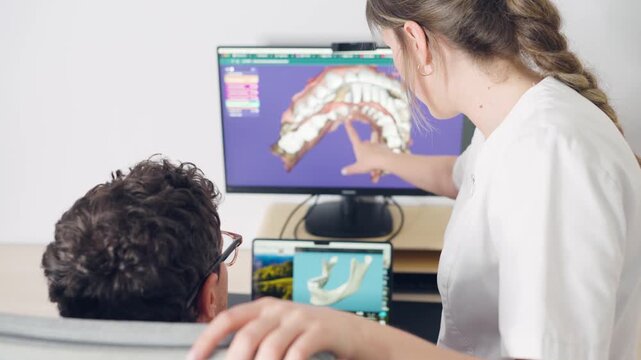 Female orthodontist discussing a treatment plan with a male patient, pointing at a 3d digital model of his teeth and jaw on a monitor