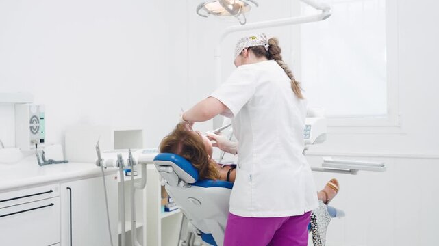 Professional female dentist in a bright, modern clinic treating a patient sitting in a dental chair during a routine oral hygiene checkup