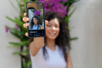 Young woman holding up a smartphone, showing herself smiling on the screen