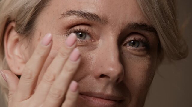 Close up of smiling woman looking into camera, smiling while massaging face with cream