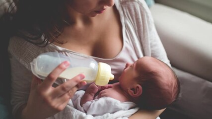 Mother feeding newborn baby bottle milk gently holding infant in warm embrace showing tender care nurturing moment bonding comfort early childhood parenting love softness calm emotion scene