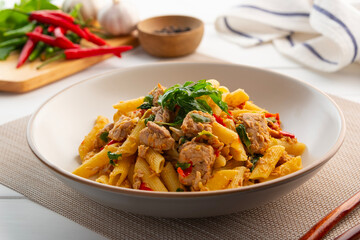 Stir fried penne pasta with Canned tuna fish and crispy basil leaves in white plate,Spicy pasta Pad Kra Pao.Thai fusion food