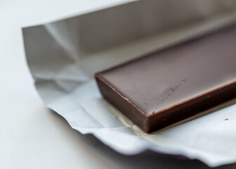 Close-up shot of a dark chocolate bar partially unwrapped in white foil on a clean light surface.
