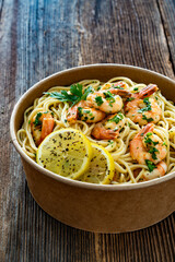 Takeaway food - fried shrimps with noodles and lemon in lunch box to go on wooden table
