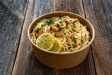 Takeaway food - fried shrimps with noodles and lemon in lunch box to go on wooden table
