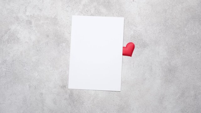 Red heart-shaped decorations scattered on a textured surface, transitioning to a blank card partially revealed, showcasing a romantic theme with copy space for Valentine's Day greetings and messages