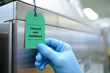 Gloved hand attaches green cleaned and validated tag to stainless steel equipment.
