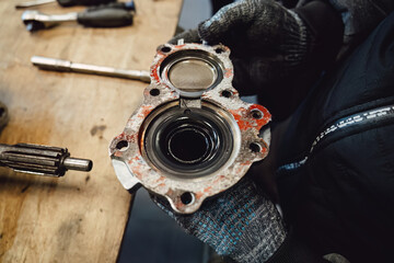 Disassembled old car gearbox with gears and tools on a workbench in an auto service garage. Repair, maintenance, and replacement of worn mechanical transmission parts in a vehicle.