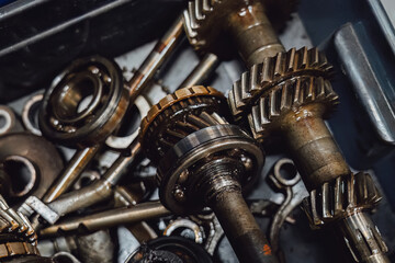 Oily transmission details: broken gearbox unit and green bin with spare parts. Close up of worn out mechanism before overhaul or recycling. Industrial grunge texture and mechanical defects.