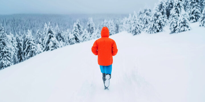 Person with a vibrant orange jacket running through fresh snow, exploring a snowy mountain path with pine trees - Powered by Adobe