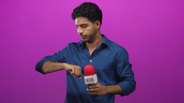 Man in blue shirt holding news microphone checks wristwatch while looking down in studio; professional focus.