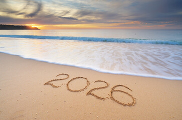 2026 year text symbol on the sea sand beach shore during sunset.
