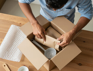 A man is unpacking a cardboard box at home, revealing a pan and kitchen items. The scene captures the excitement of opening a delivery and organizing new kitchen essentials