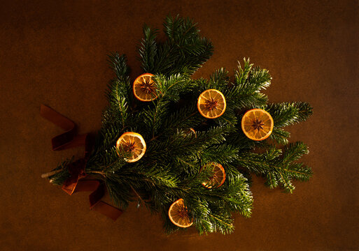 Bouquet de No&euml;l en branches de sapin vert nou&eacute; d'un ruban en velours brun orang&eacute;, d&eacute;cor&eacute; avec des tranches d'oranges s&eacute;ch&eacute;es et d'anis &eacute;toil&eacute;, vue du dessus sur un fond marron