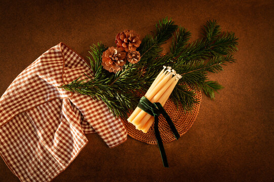 D&eacute;coration de table de No&euml;l vue du dessus, branche de sapin vert, bougies naturelles, ruban en velours vert, pommes de pin, serviette en tissu &agrave; carreaux brun, fond marron