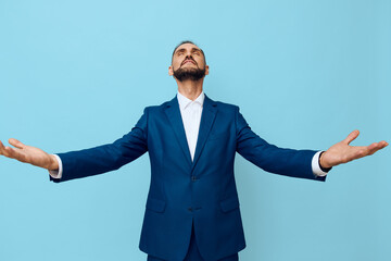 A confident business professional stands alone against a solid blue background, arms open wide, exuding triumph and gratitude in a calm, focused mood.
