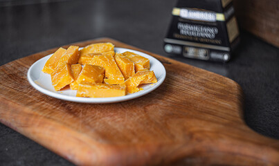 A refined serving of aged hard cheese rests on a pristine white plate atop a rich wooden countertop. Elegant gourmet styling with warm, artisanal texture and premium culinary ambiance