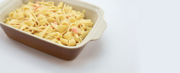 Teglia in terracotta con pasta alla panna e salmone in primo piano su superficie bianca