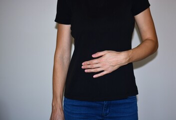 Woman touching upper abdomen with a single hand, illustrating stomach pain, digestion problems, acid reflux or nausea. Concept of discomfort, health issues and medical symptoms.